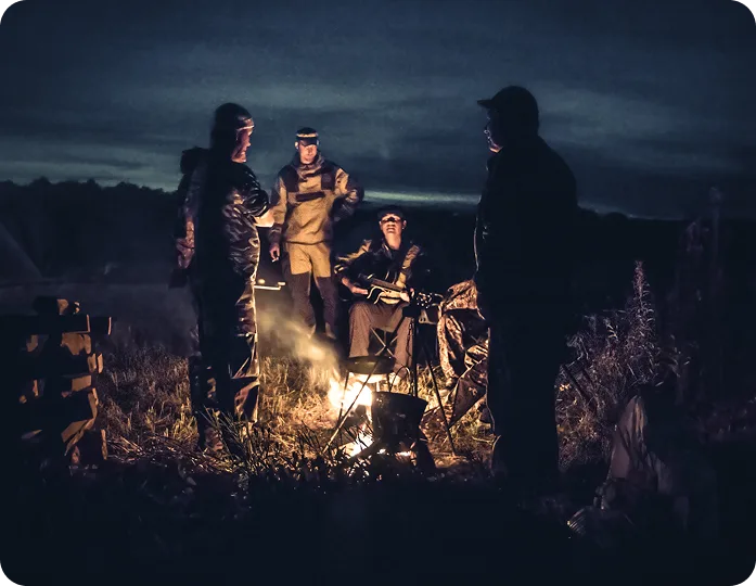 Four people around a campfire at night, sharing stories and music.